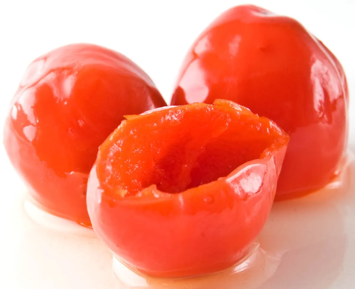 Three whole piquanté peppers, one split open to show the hollow, cherry-sized flesh.